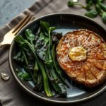 Lions Mane steak with olive butter and bitter greens on a dark ceramic plate